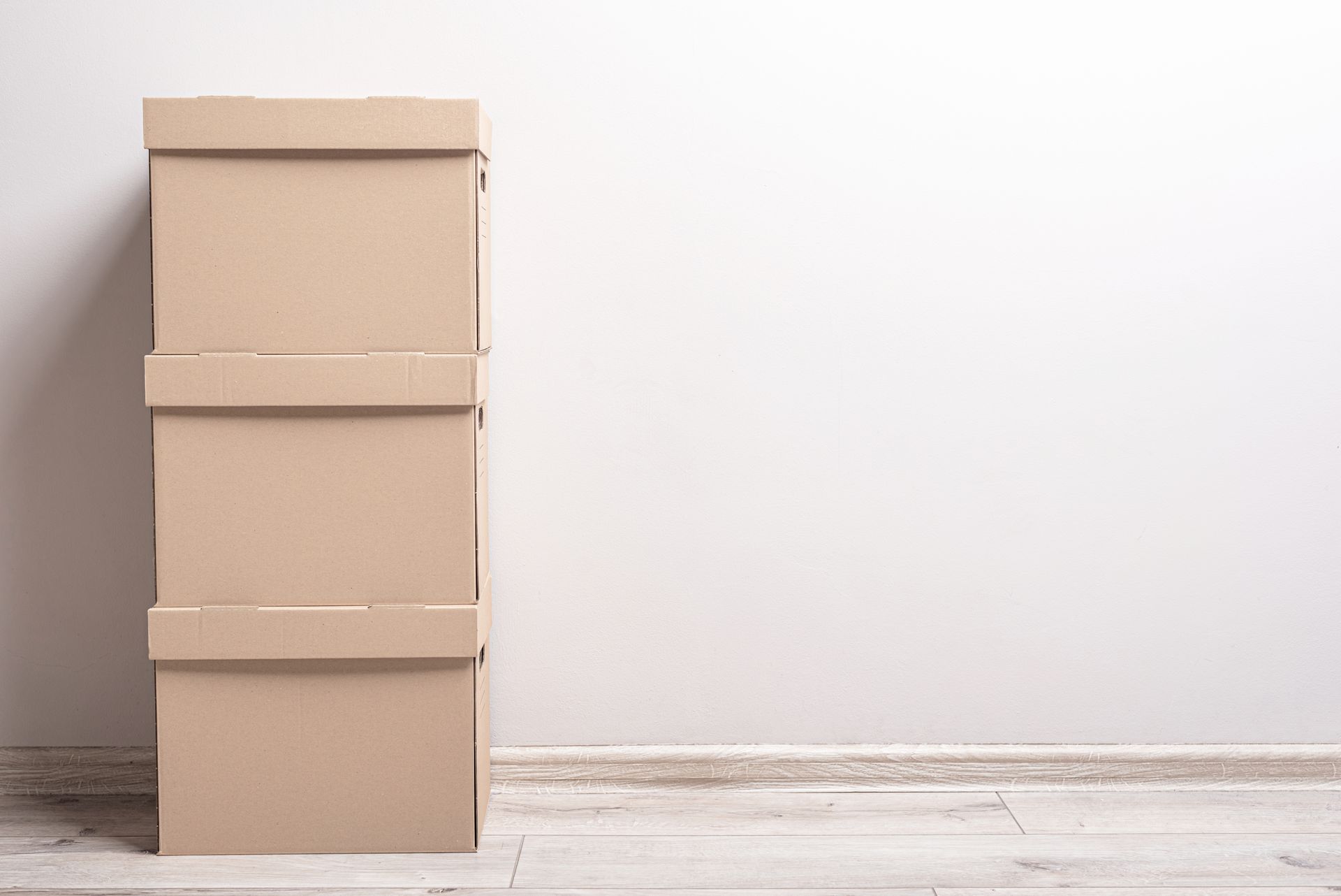 Three stacked cardboard boxes against a white wall and wooden floor.