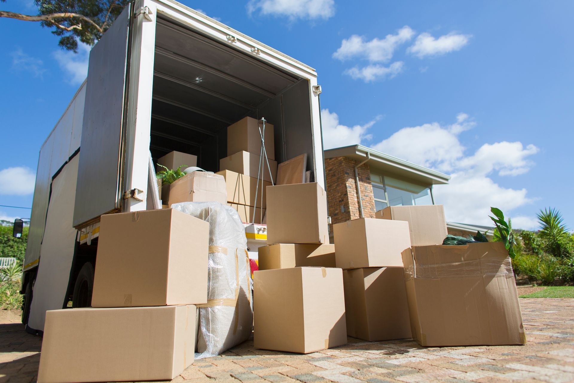 Moving boxes being loaded into a truck in front of a house on a sunny day.